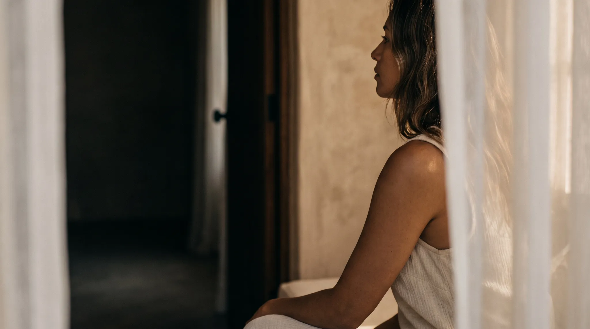 A woman in quiet profile behind a sheer curtain in soft light